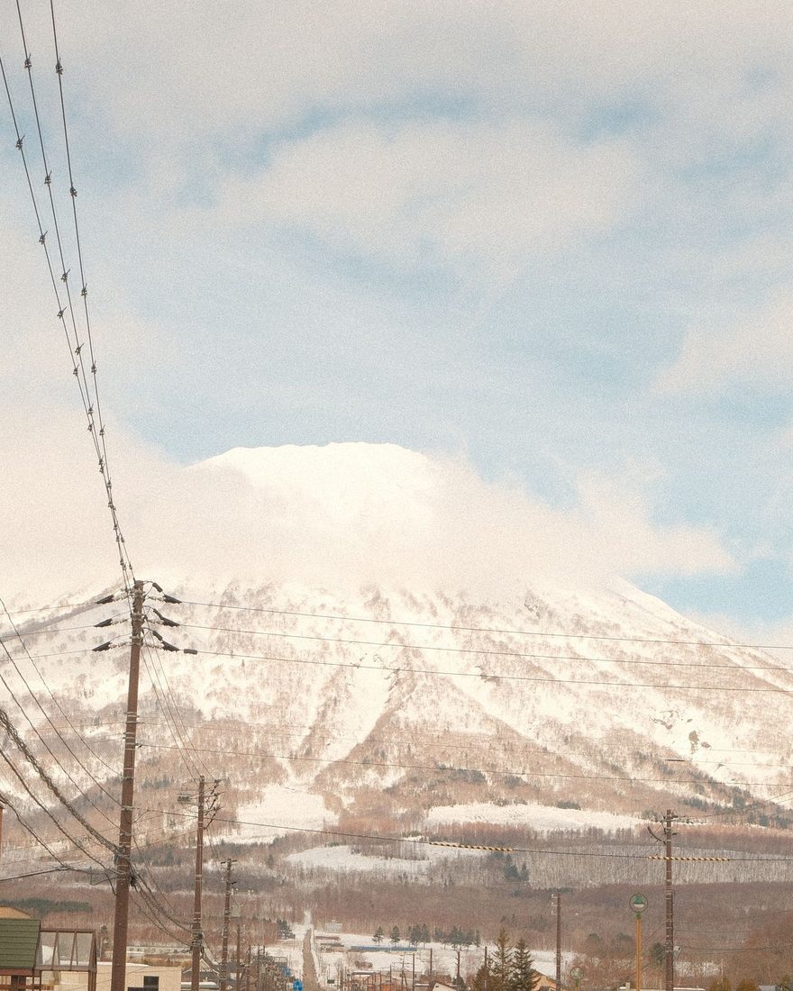 雪をかぶった大きな山へまっすぐ続く、北海道の町の通りと電線